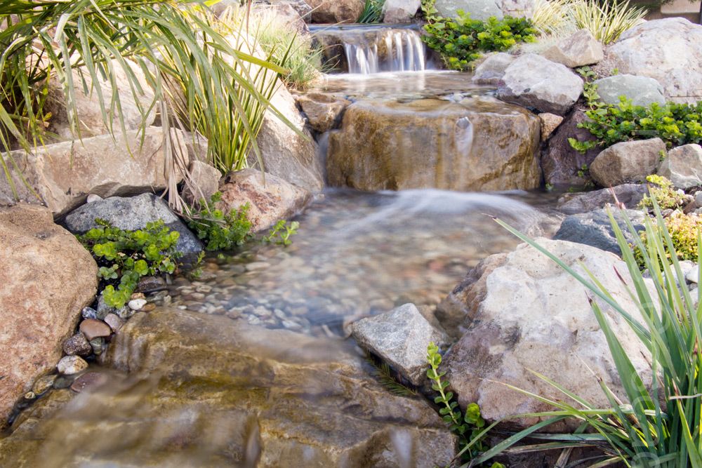 Close-up stream. This is a premium rock iption which costs 3 x more than standard rocks but looks spectacular. A stream makes an excellent interactive feature for toe dangling whilst enjoying your favourite tipple. This design was also pondless for absolute minimal maintenance.  - Landscaping and Water Features -  Creative Cascades